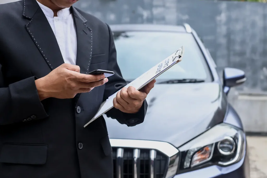 Car buyer checking invoice price information on a clipboard and phone before purchasing a vehicle