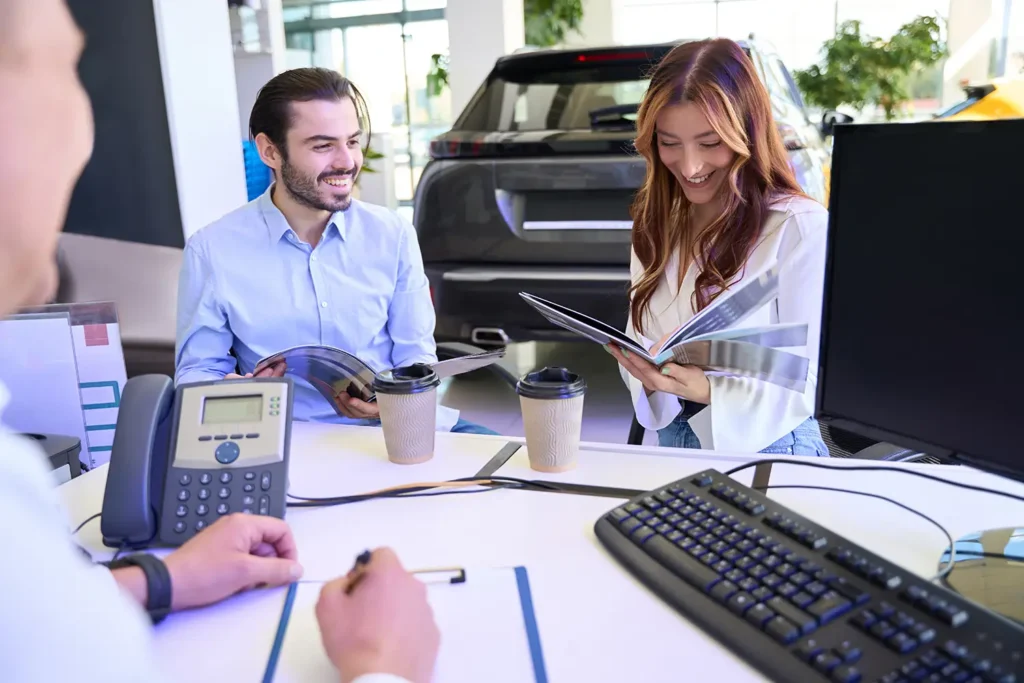 Couple reviewing vehicle pricing information with a salesperson at a car dealership
