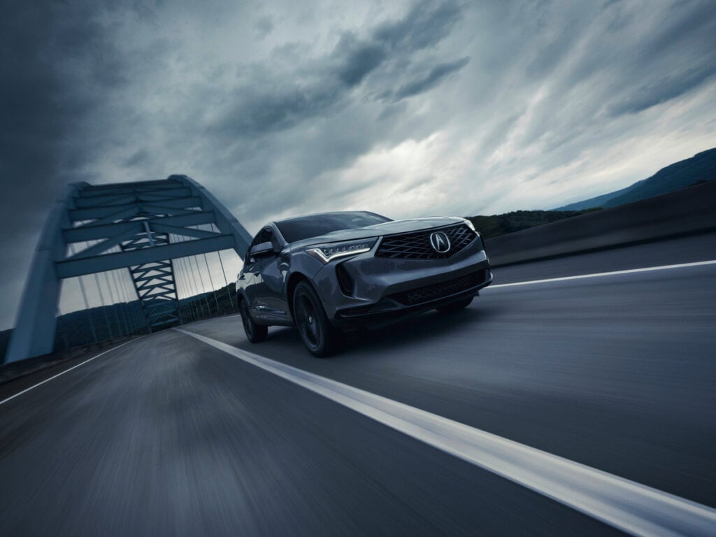 Acura RDX Review image of an Acura RDX driving on a highway bridge under a dramatic cloudy sky.