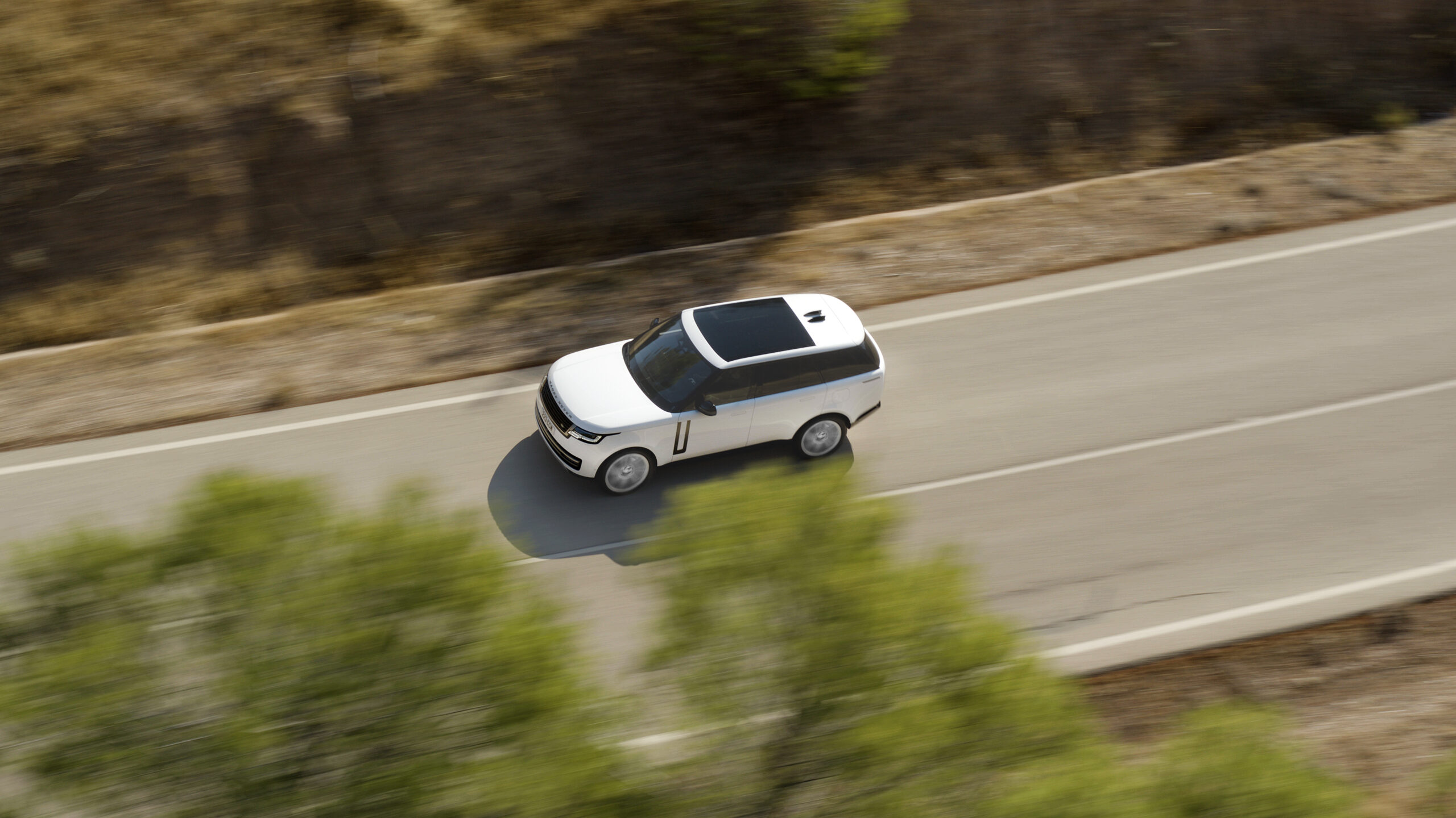 White Range Rover luxury SUV driving on a paved road in an overhead view for a Range Rover Review.