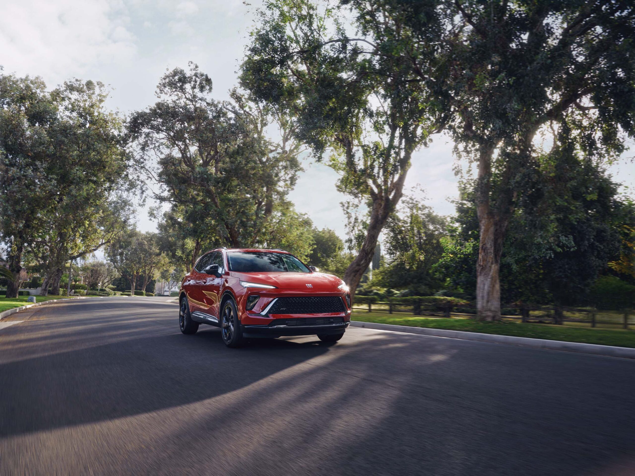 Red Buick Envision driving on a tree-lined road in daylight, featured in our Buick Envision Review.