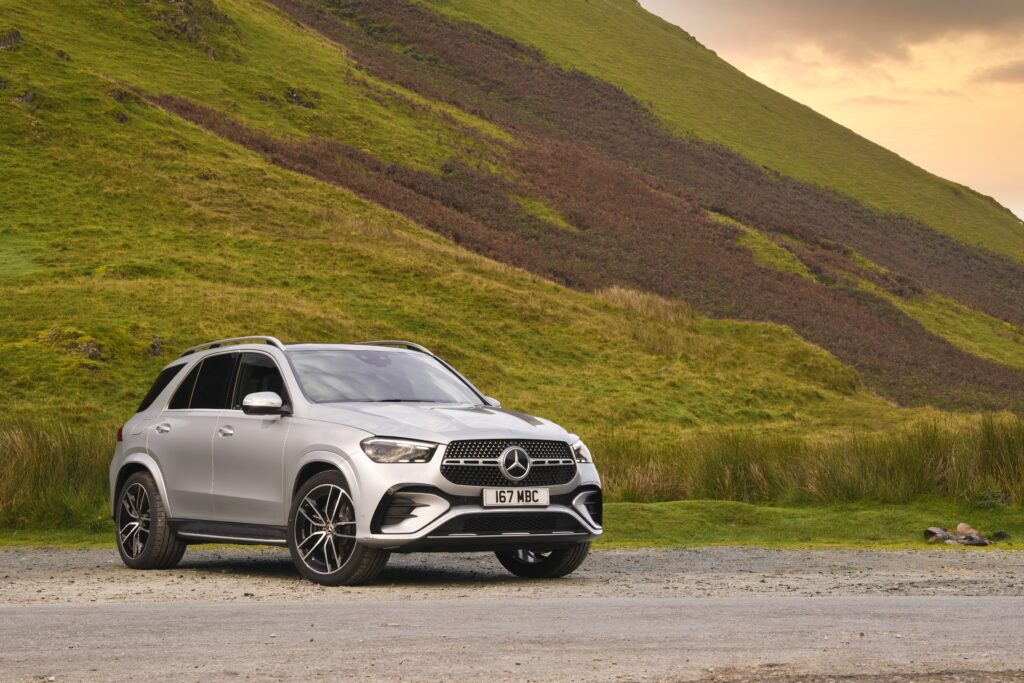 Silver Mercedes-Benz GLE luxury SUV parked in front of green hills and open countryside for a Mercedes-Benz GLE Review.
