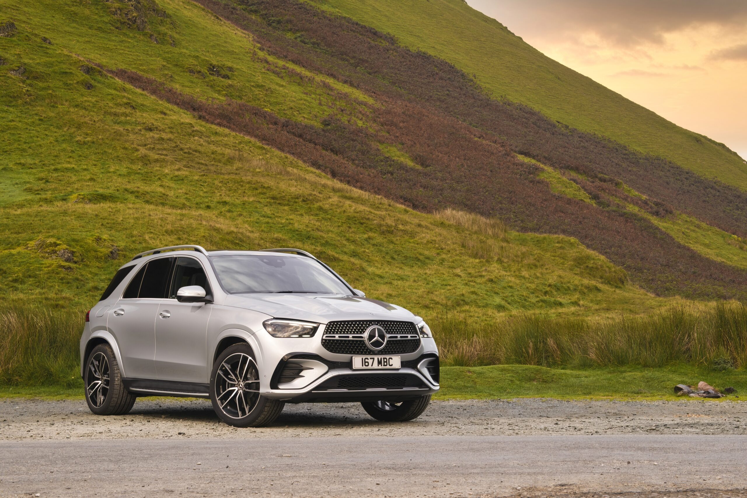 Silver Mercedes-Benz GLE luxury SUV parked in front of green hills and open countryside for a Mercedes-Benz GLE Review.