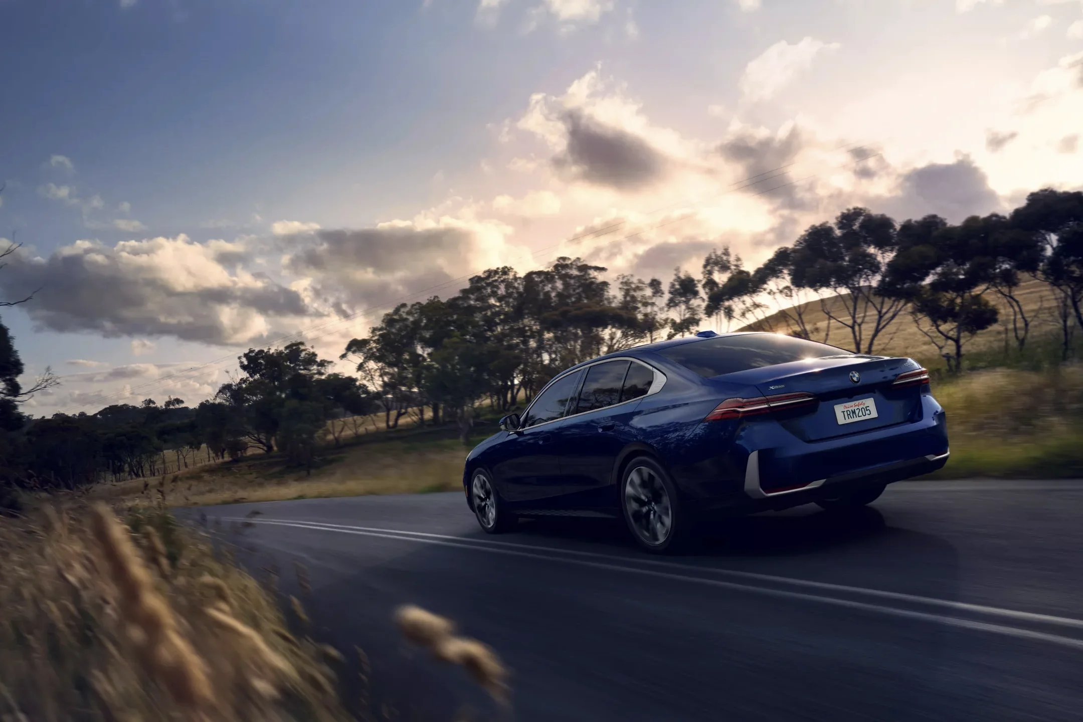 A blue BMW 5 Series driving on a two-lane road at sunset, shown in our BMW 5 Series Review.