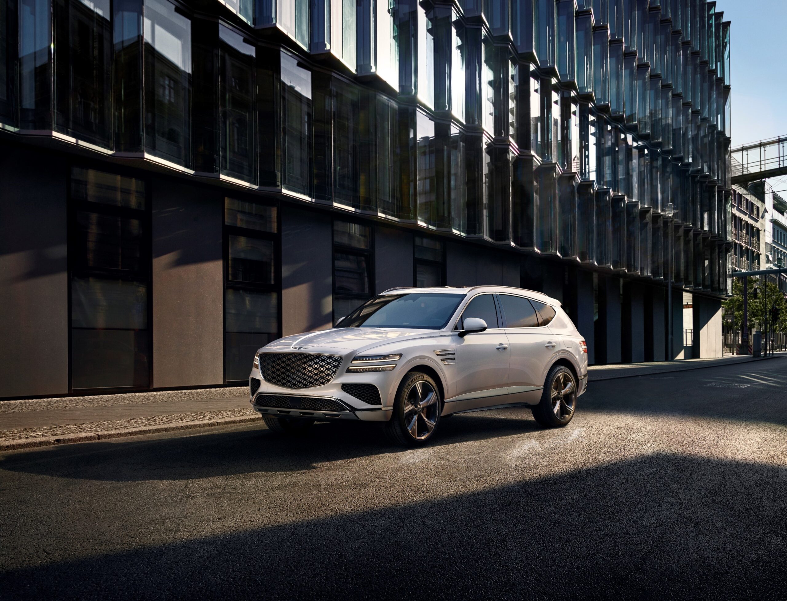 White Genesis GV80 luxury SUV parked on a city street beside modern glass buildings for a Genesis GV80 Review.