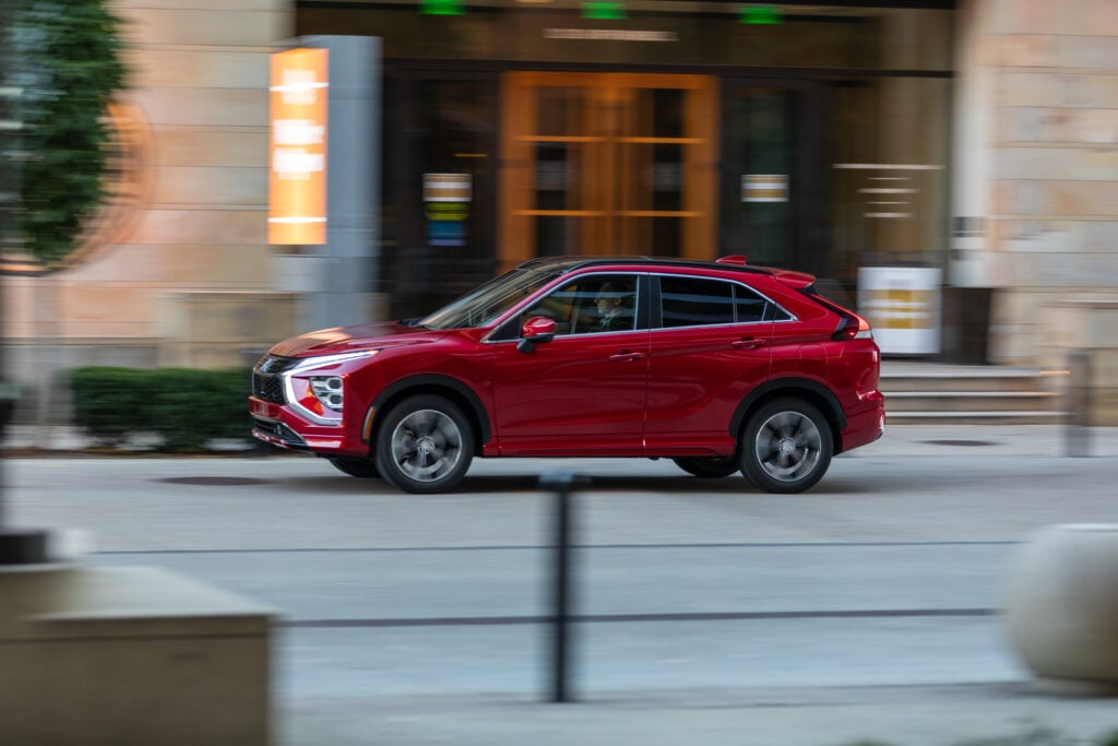 Red Mitsubishi Eclipse Cross driving through a city street in side profile for a Mitsubishi Eclipse Cross Review.