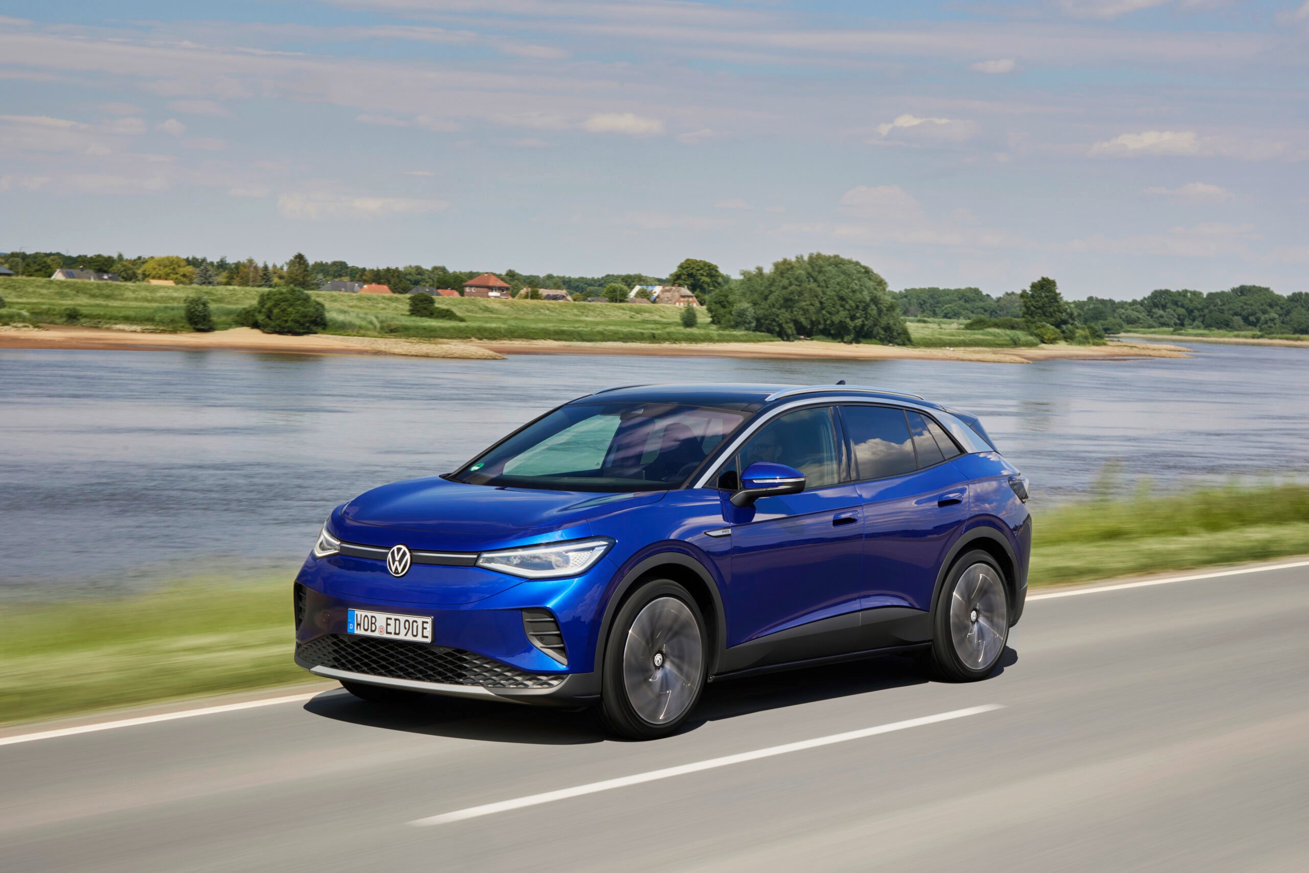 Blue Volkswagen ID.4 electric SUV driving on a road beside a river for a Volkswagen ID.4 Review.