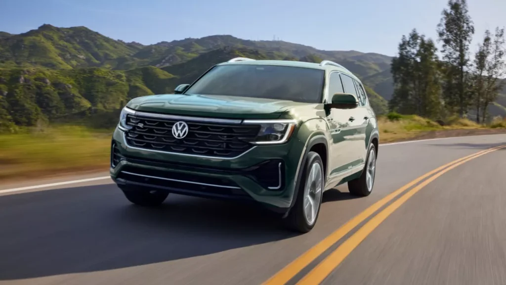 Green Volkswagen Atlas SUV driving on a two-lane road with mountains in the background for a Volkswagen Atlas Review.