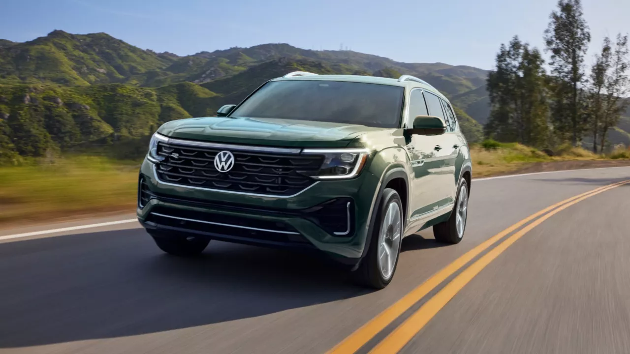 Green Volkswagen Atlas SUV driving on a two-lane road with mountains in the background for a Volkswagen Atlas Review.