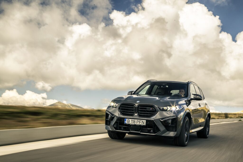 A BMW X5 driving on a desert road at sunset with lens flare, featured in our BMW X5 Review.