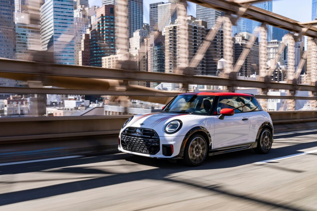 White MINI Cooper 2 Door driving across a city bridge with a skyline in the background for a MINI Cooper 2 Door Review.