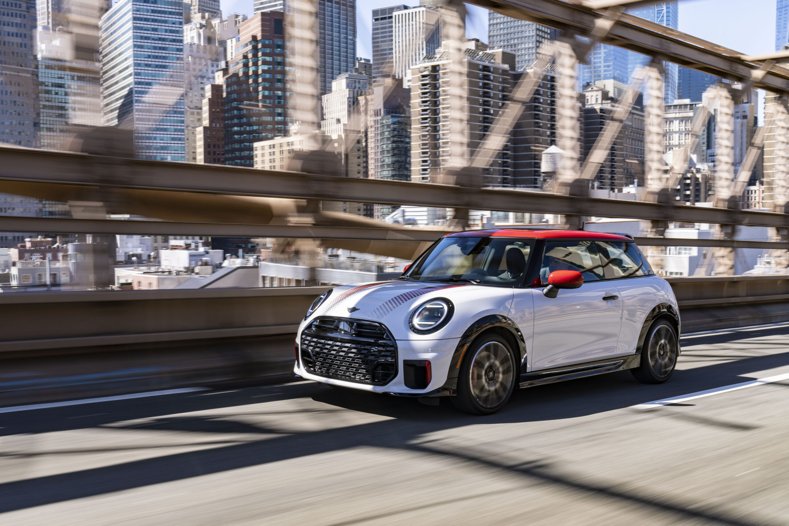 White MINI Cooper 2 Door driving across a city bridge with a skyline in the background for a MINI Cooper 2 Door Review.