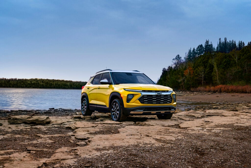 2026 Chevrolet Trailblazer in yellow parked on rocky terrain near a lake with forest in the background