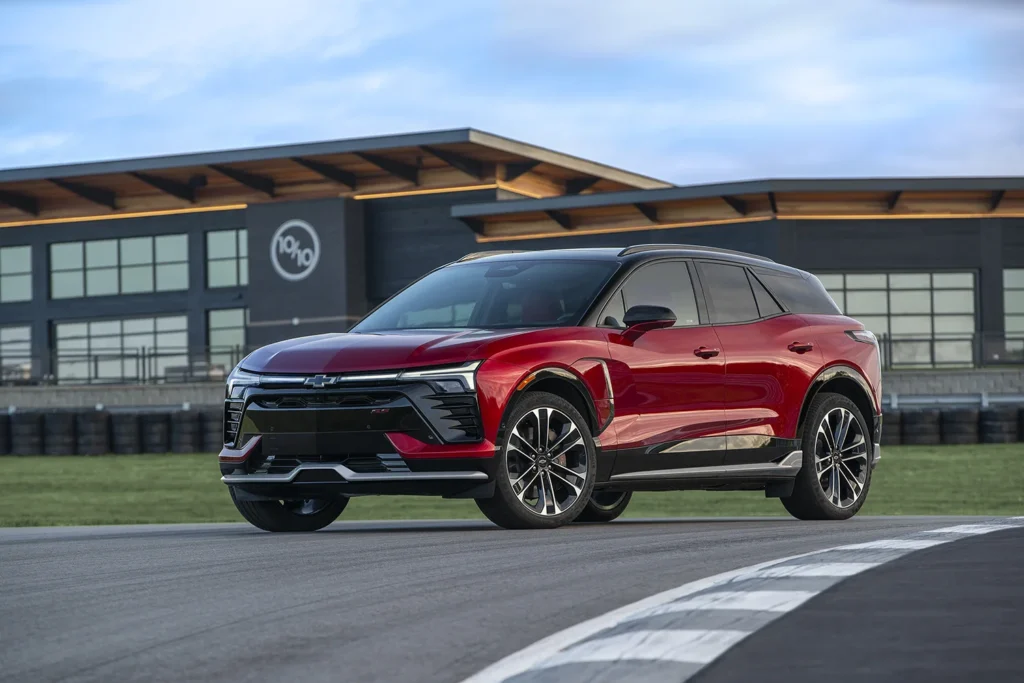 2026 Chevrolet Blazer EV SS in Radiant Red Tintcoat with black roof parked on a race track with tire barriers and a modern facility building in the background