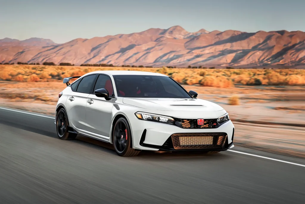 2026 Honda Civic Type R in Championship White with bronze lower grille, rear wing, and red brake calipers driving at speed on a desert highway with mountains in the background
