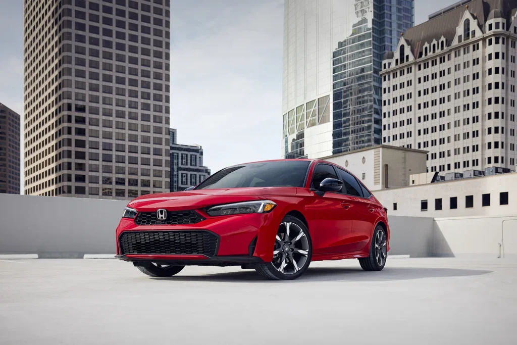 2026 Honda Civic Hybrid Sedan Sport Touring in Rallye Red parked on a rooftop with a downtown city skyline and tall buildings visible in the background