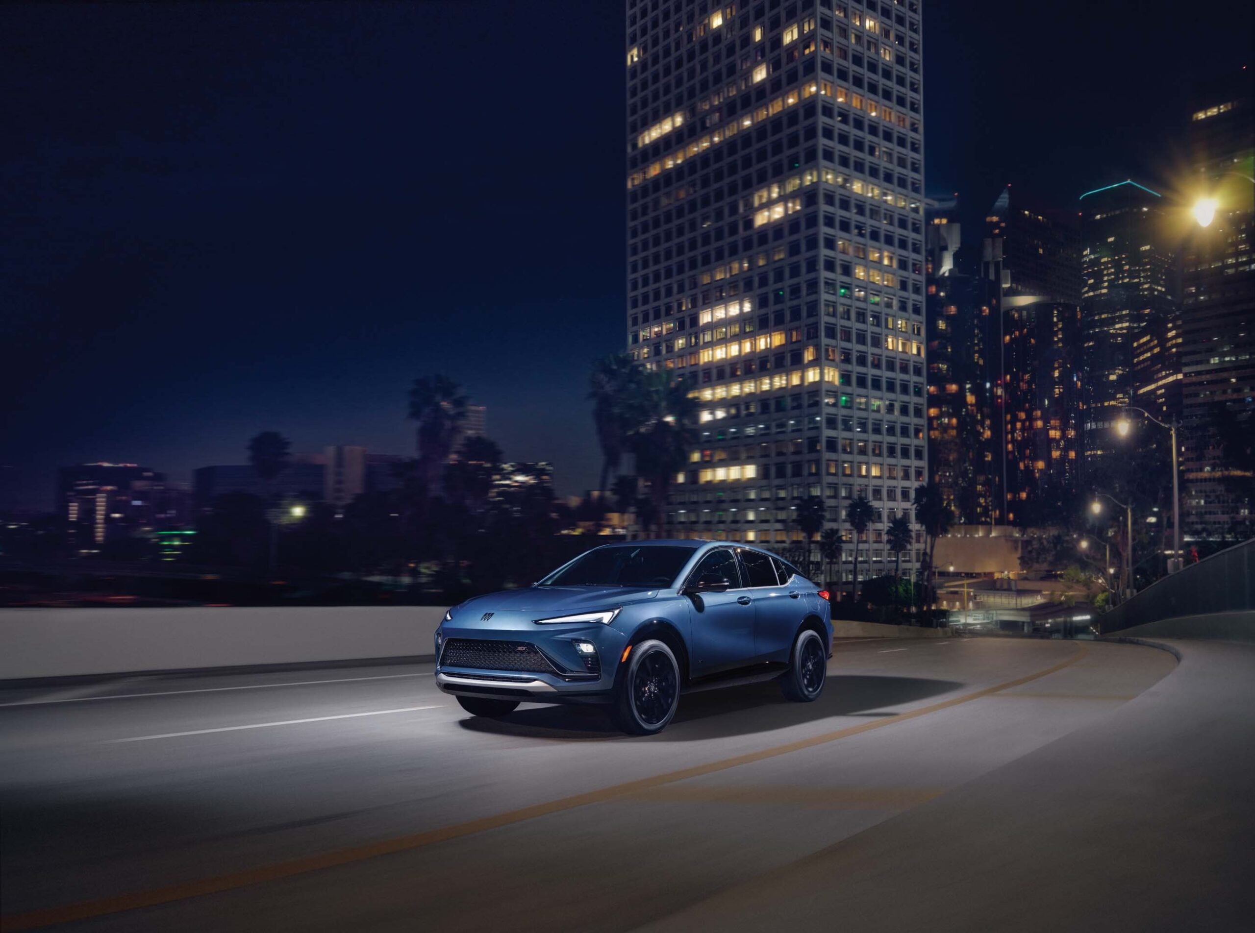 2026 Buick Envista in dark blue metallic parked on an urban street showcasing its fastback coupe silhouette and swept-back roofline