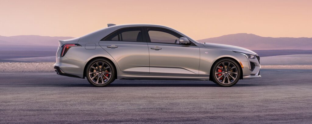 2026 Cadillac CT4 Sport in Coastal Blue Metallic driving on an open road with city skyline in the background
