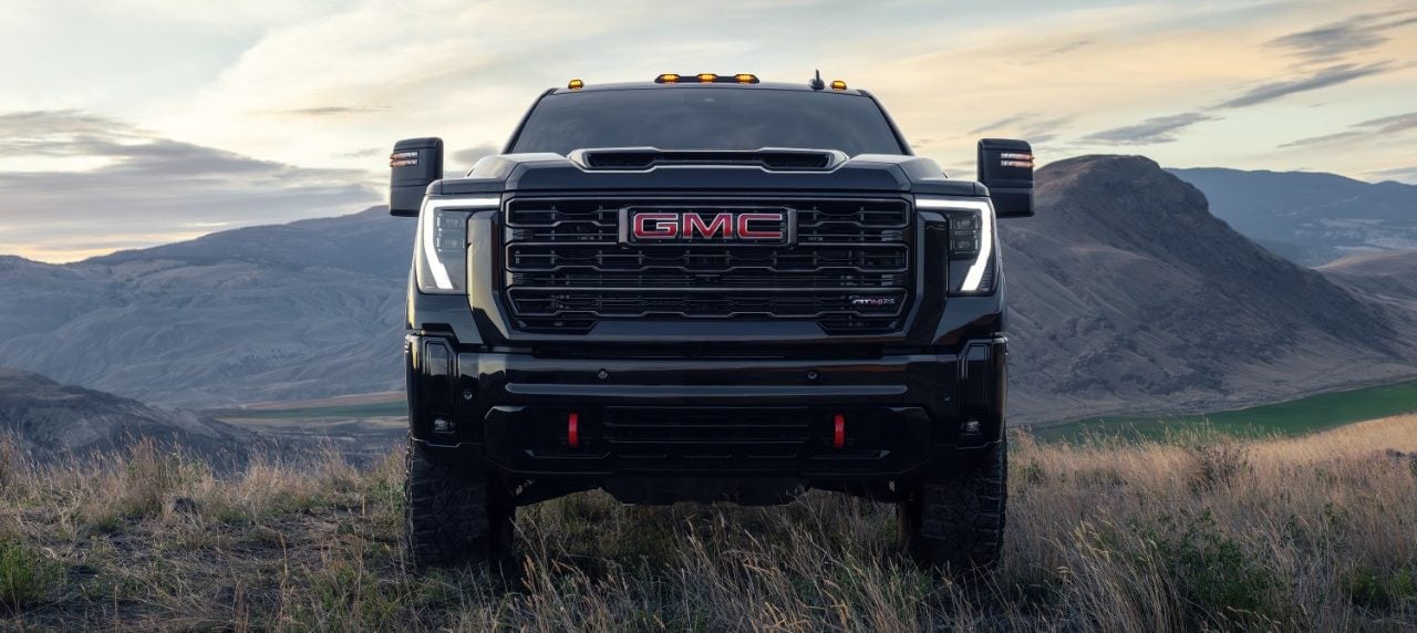 2025 GMC Sierra HD AT4X in Onyx Black facing forward on a hilltop with mountain range and dramatic sky in the background