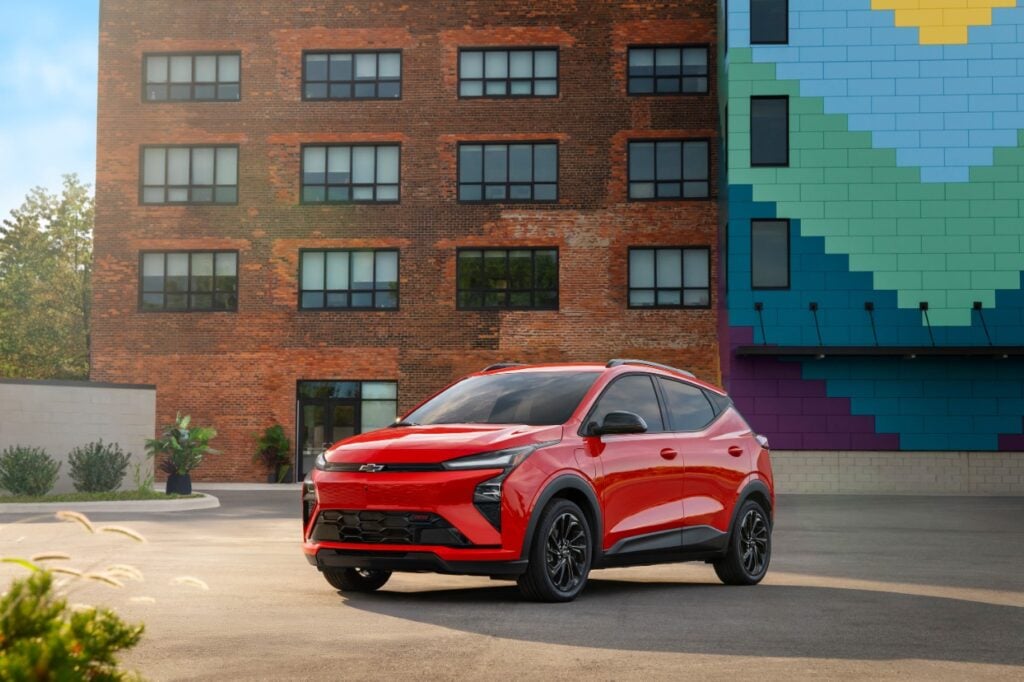 Red 2027 Chevrolet Bolt RS parked in front of a brick building with a colorful mural