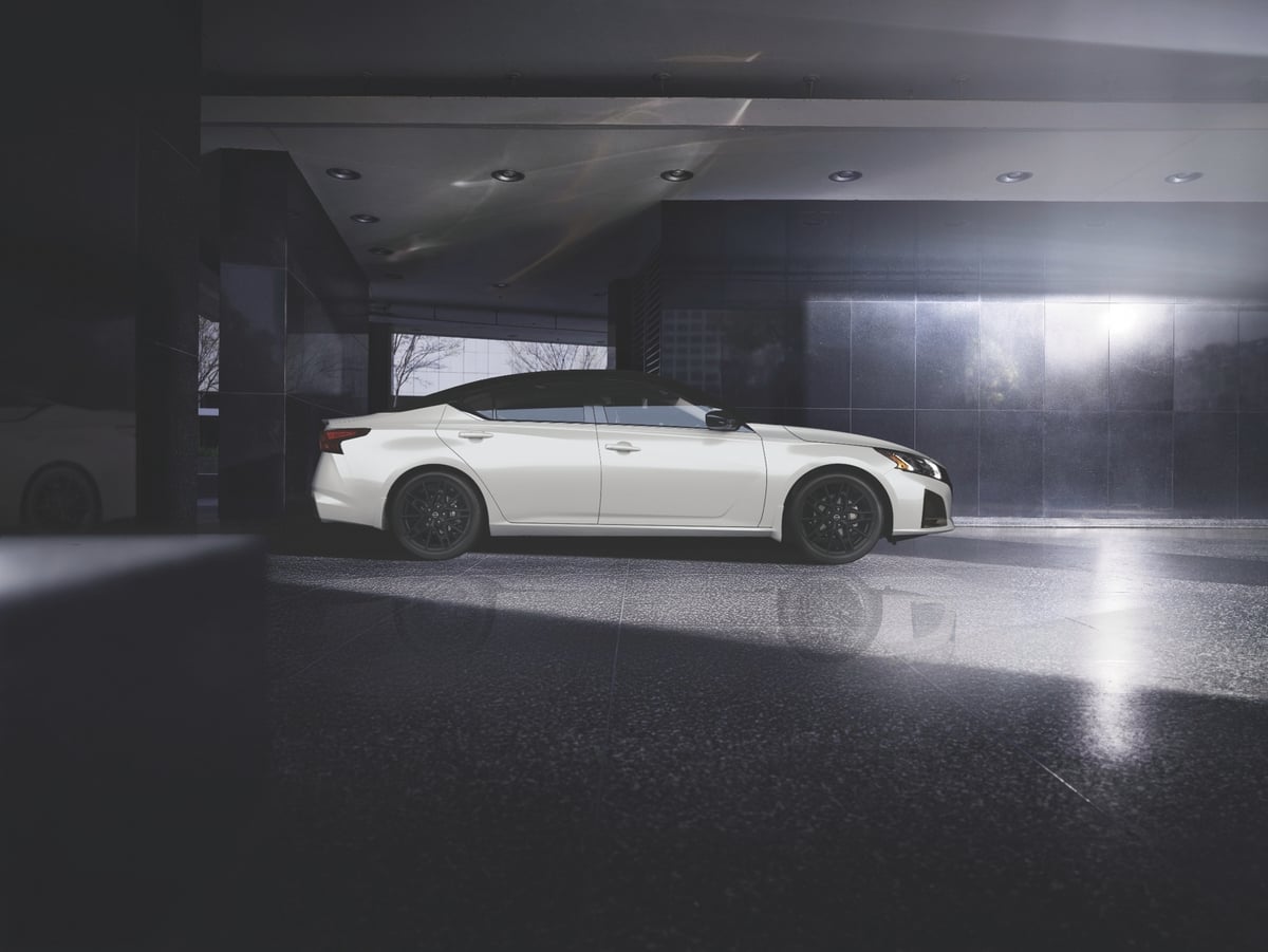 White 2026 Nissan Altima sedan shown in side profile, parked in a dark garage with dramatic overhead lighting