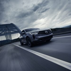 Acura RDX Review image of an Acura RDX driving on a highway bridge under a dramatic cloudy sky.