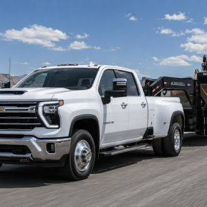 2026 Chevrolet Silverado 3500HD Crew Cab DRW in white towing a Caterpillar track loader on an IronBull gooseneck trailer on a desert highway