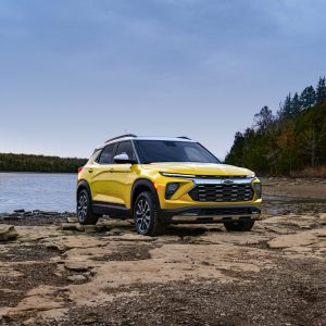 2026 Chevrolet Trailblazer in yellow parked on rocky terrain near a lake with forest in the background