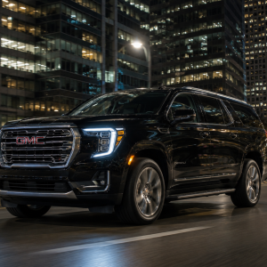 2026 GMC Yukon XL Denali in Onyx Black driving through a downtown city street at night with illuminated skyscrapers in the background