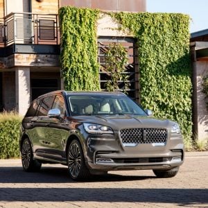 Gray Lincoln Aviator luxury SUV parked outside a modern home with greenery in the background for a Lincoln Aviator Review.