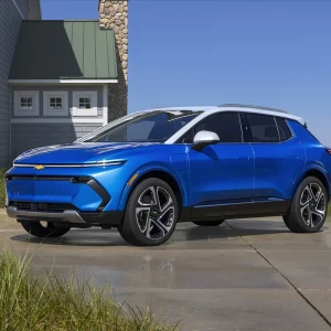 2026 Chevrolet Equinox EV in Riptide Blue Metallic with white roof parked on a coastal driveway with ocean and beach grass in the background