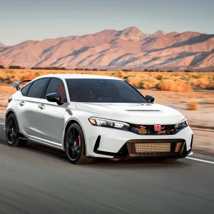 2026 Honda Civic Type R in Championship White with bronze lower grille, rear wing, and red brake calipers driving at speed on a desert highway with mountains in the background