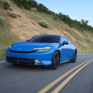 2026 Honda Prelude in Boost Blue Pearl taking a curve on a mountain road at speed with a dry hillside and trees visible in the background