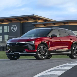 2026 Chevrolet Blazer EV SS in Radiant Red Tintcoat with black roof parked on a race track with tire barriers and a modern facility building in the background