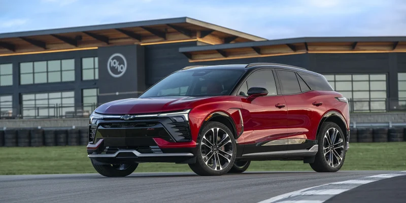 2026 Chevrolet Blazer EV SS in Radiant Red Tintcoat with black roof parked on a race track with tire barriers and a modern facility building in the background