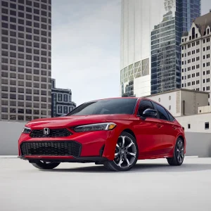 2026 Honda Civic Hybrid Sedan Sport Touring in Rallye Red parked on a rooftop with a downtown city skyline and tall buildings visible in the background
