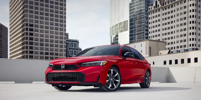 2026 Honda Civic Hybrid Sedan Sport Touring in Rallye Red parked on a rooftop with a downtown city skyline and tall buildings visible in the background