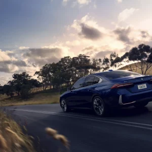 A blue BMW 5 Series driving on a two-lane road at sunset, shown in our BMW 5 Series Review.