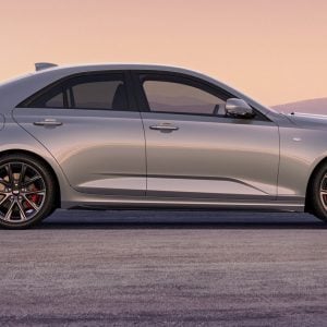 2026 Cadillac CT4 Sport in Coastal Blue Metallic driving on an open road with city skyline in the background