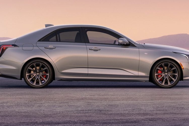 2026 Cadillac CT4 Sport in Coastal Blue Metallic driving on an open road with city skyline in the background