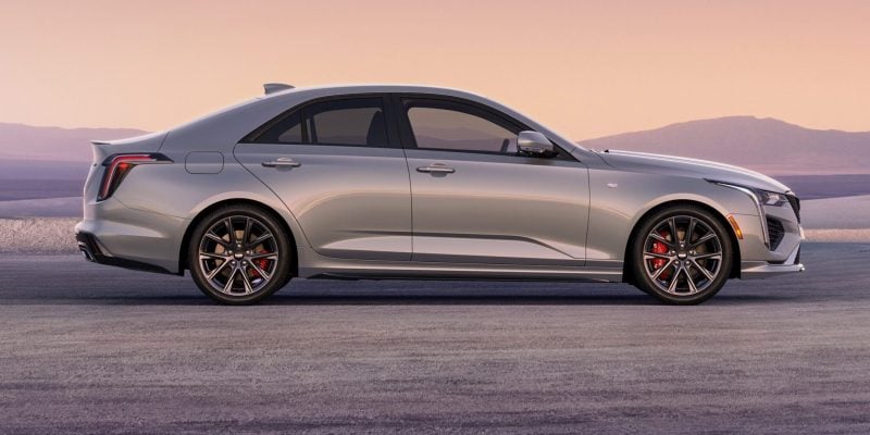 2026 Cadillac CT4 Sport in Coastal Blue Metallic driving on an open road with city skyline in the background