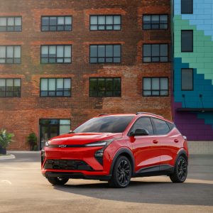 Red 2027 Chevrolet Bolt RS parked in front of a brick building with a colorful mural