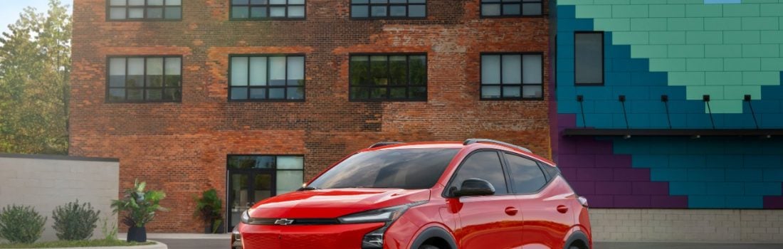 Red 2027 Chevrolet Bolt RS parked in front of a brick building with a colorful mural