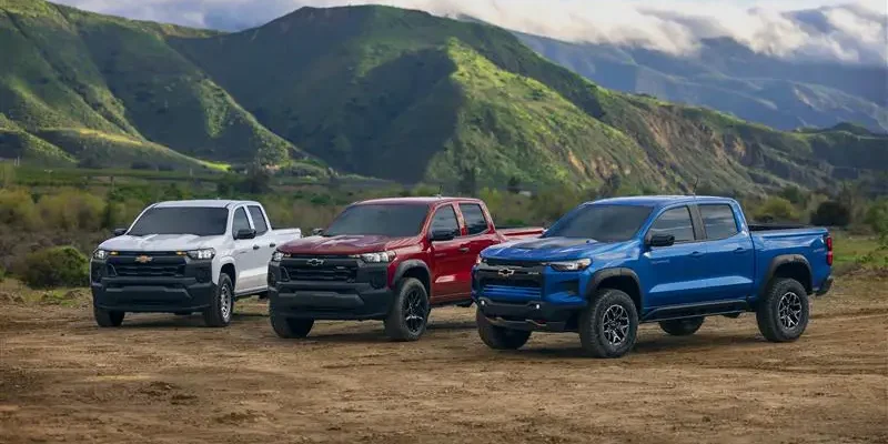 Three 2026 Chevrolet Colorado pickup trucks parked off-road with mountains in the background.