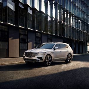 White Genesis GV80 luxury SUV parked on a city street beside modern glass buildings for a Genesis GV80 Review.
