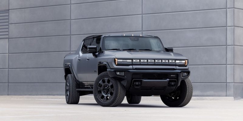 2026 GMC HUMMER EV Pickup in Moonstone Gray parked on rugged terrain with mountains in the background