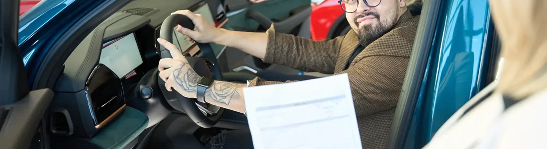 Man sitting in a new car during a dealership visit, reviewing paperwork related to Invoice Price vs. MSRP.