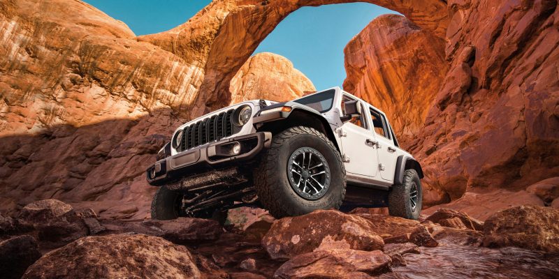 White 2026 Jeep Wrangler climbing over rocks in a desert canyon landscape