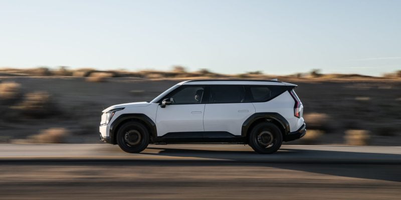2026 Kia EV9 three-row electric SUV in white parked on a scenic road showing its bold exterior design