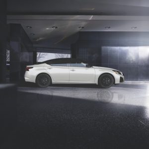 White 2026 Nissan Altima sedan shown in side profile, parked in a dark garage with dramatic overhead lighting